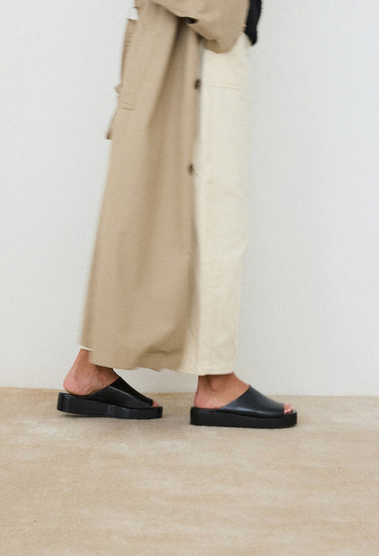 Person wearing beige pants and the black Lido slide sandal on a neutral background