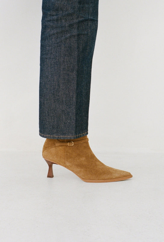 Brown suede Ilana ankle boot worn with dark jeans on a light gray background.