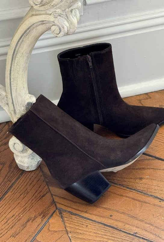 Pair of black suede ankle boots on a wooden floor with decorative wall molding.