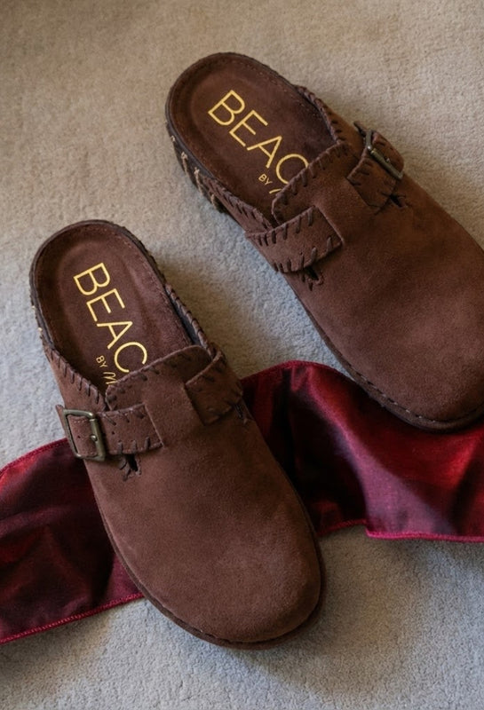Pair of brown clogs with 'BEACH' branding on a beige carpet.