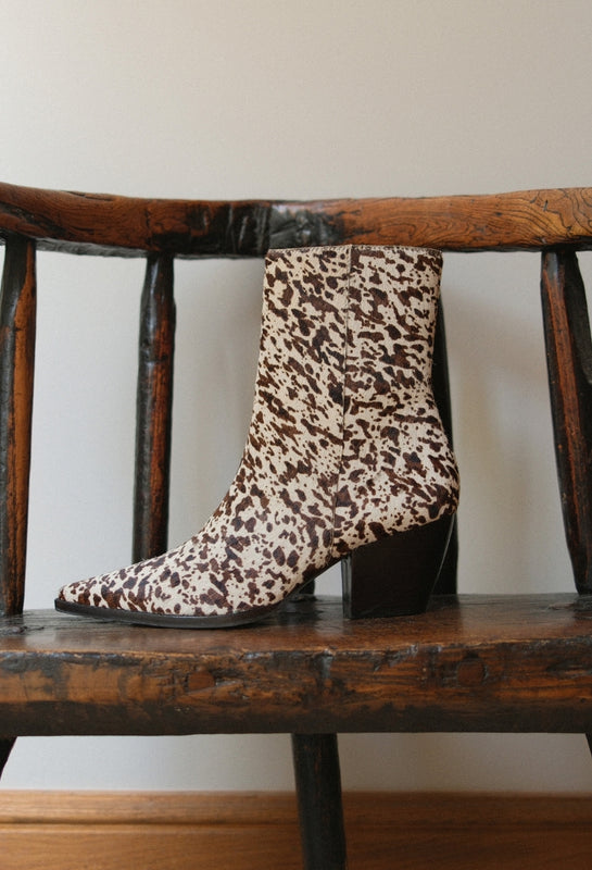 Brown and white cow print Caty Ankle Boot on a wooden chair against a white background