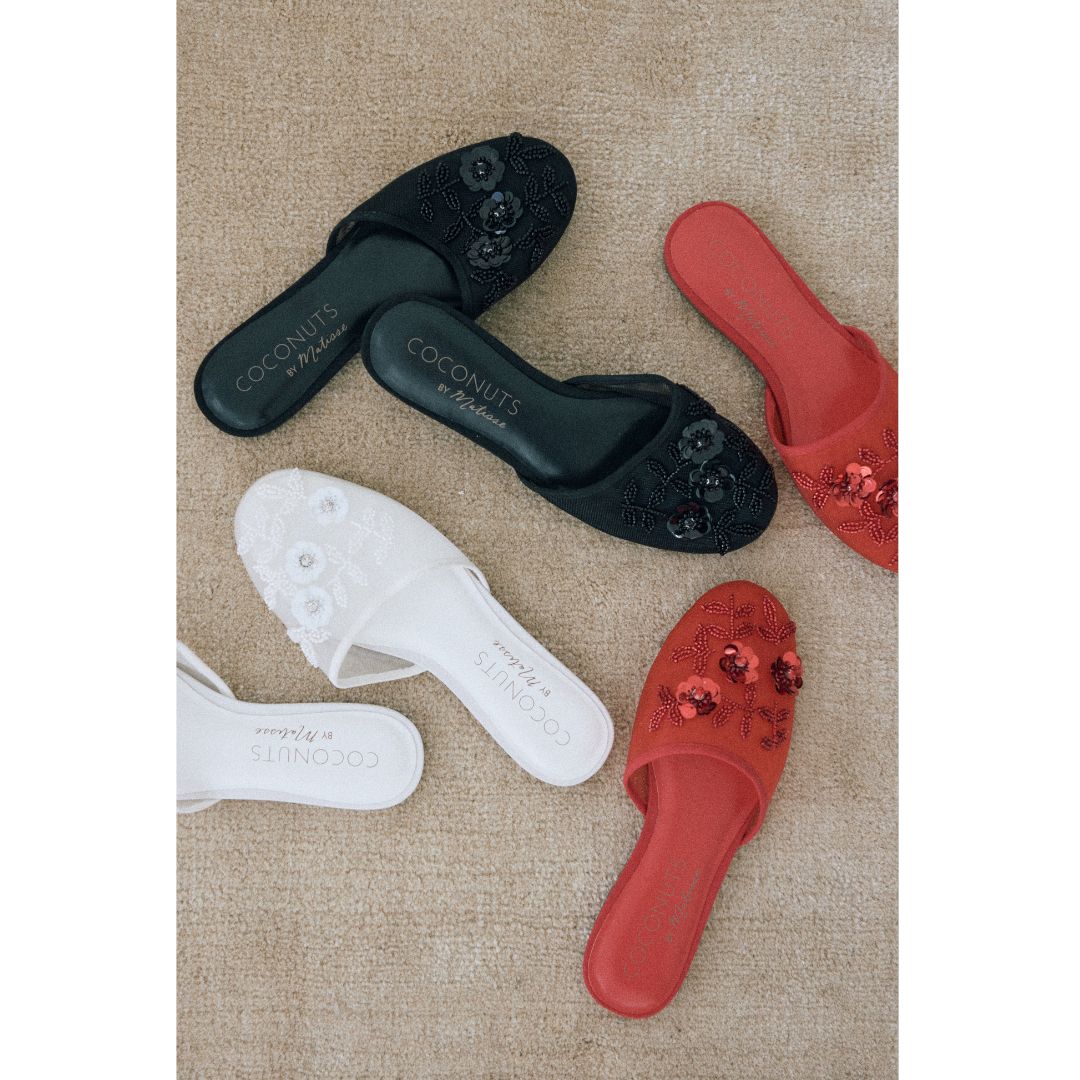 Black, white, and red embroidered slippers with 'Coconuts by Matisse' branding on a beige carpet.