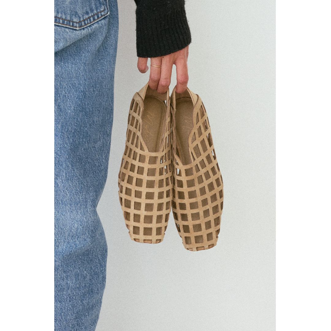 Person holding a pair of cage-style flat shoes against a plain background.