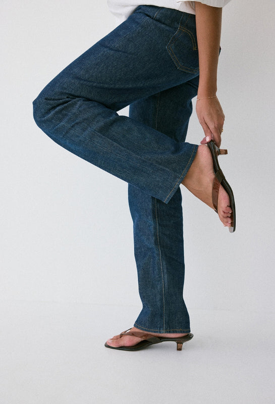 Person wearing blue jeans and a white shirt on a plain background