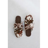Pair of brown and white cow hair slip-on shoes with brown laces on a light gray background.