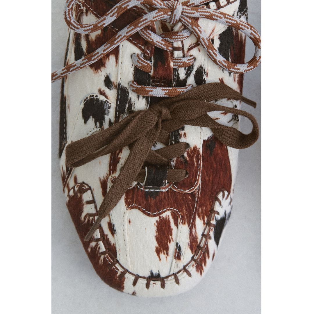 Close-up of a shoe with brown and white pattern and brown laces on a light gray background