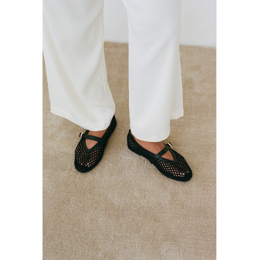 Black woven Nolita Ballet Flats worn with white pants on a beige carpet.