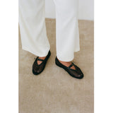Black woven Nolita Ballet Flats worn with white pants on a beige carpet.
