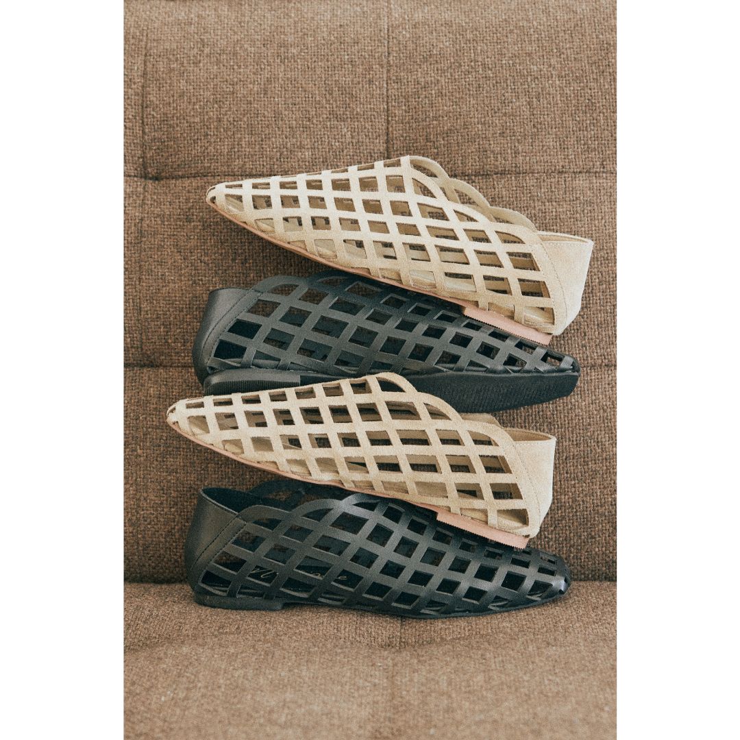 Two pairs of flat shoes with lattice designs stacked on a textured surface.