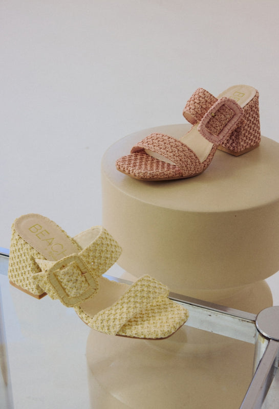 Pair of woven sandals on a round beige surface with a white background