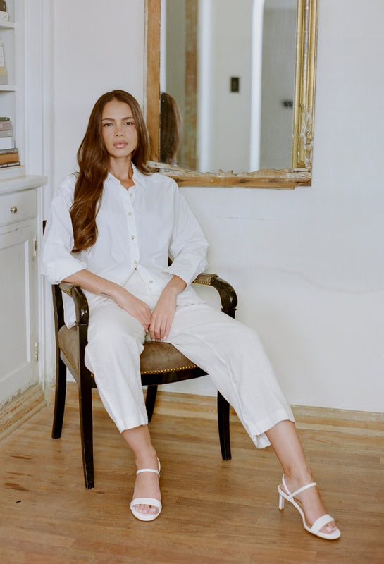 Woman in a white outfit sitting on a chair in a room with a mirror.