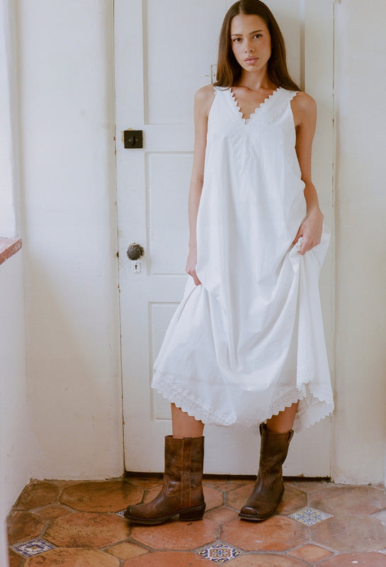 Woman wearing a white dress and brown boots standing in a room with a white door.