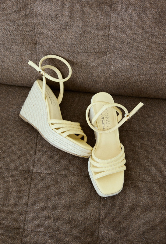 Pair of beige wedge sandals on a brown textured surface