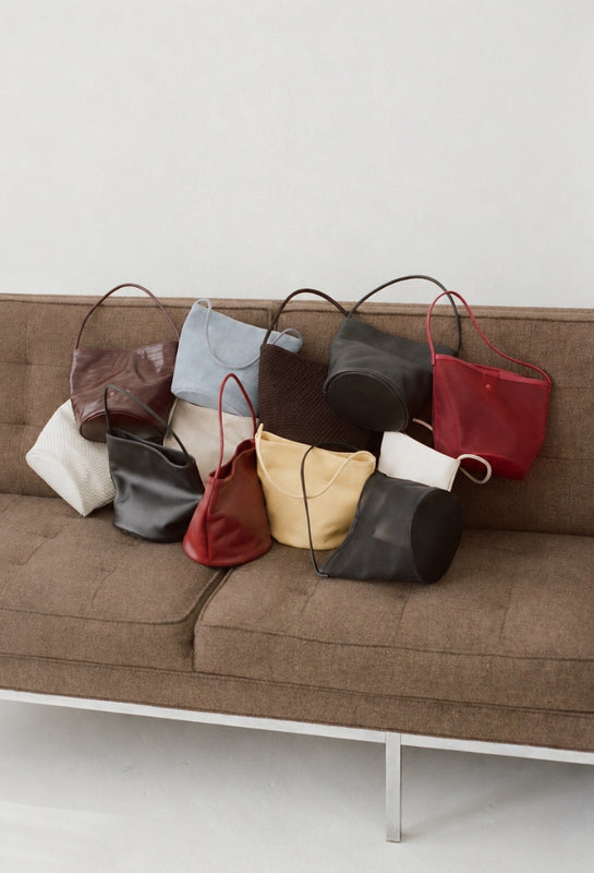Collection of handbags in various colors on a brown couch against a white background