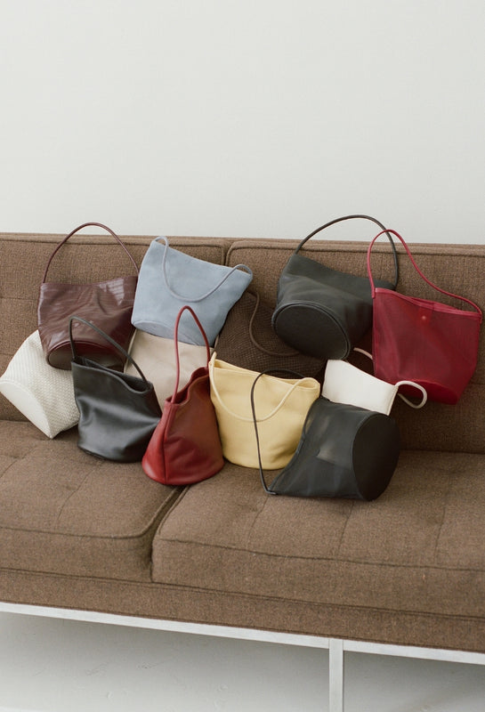 Collection of handbags in various colors on a brown couch against a white background