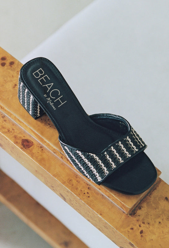 Black sandal with striped strap on a wooden surface