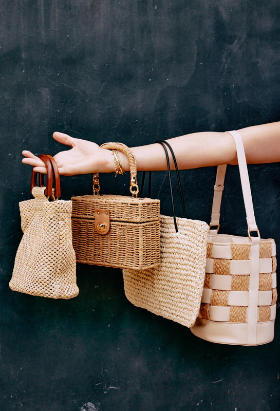Hand holding four woven bags against a dark background