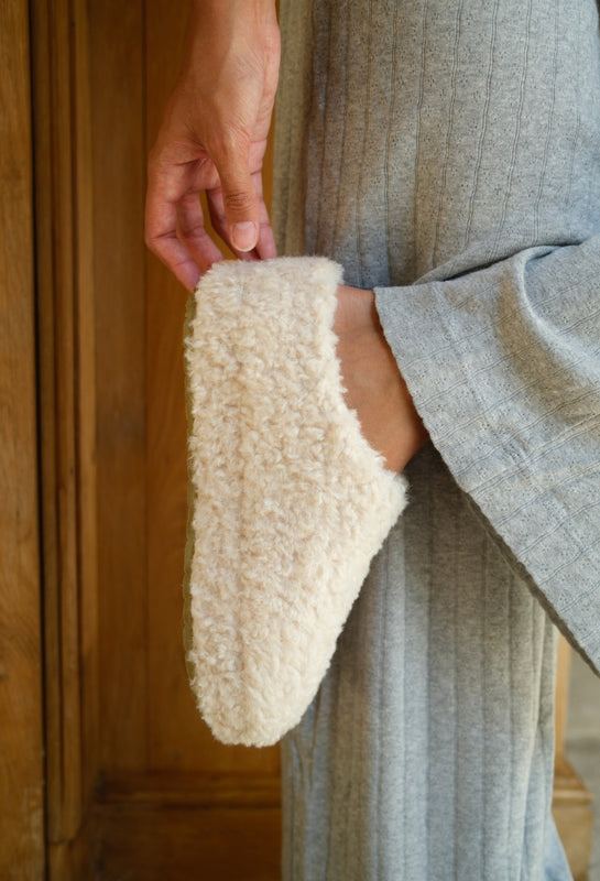 Person wearing a textured robe holding a cream-colored bathrobe over their shoulder.
