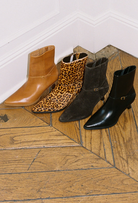 Four pairs of boots including brown, leopard print, black, and another black boot on a wooden floor.