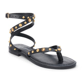 Black leather thong sandal with gold studs and wraparound ankle strap shown on a white background.
