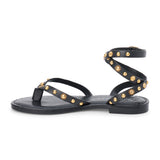 Black leather thong sandal with gold studs and wraparound ankle strap shown on a white background.