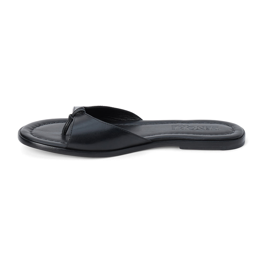 Black leather flat sandal with minimalist thong strap and padded footbed, shown on a white background.