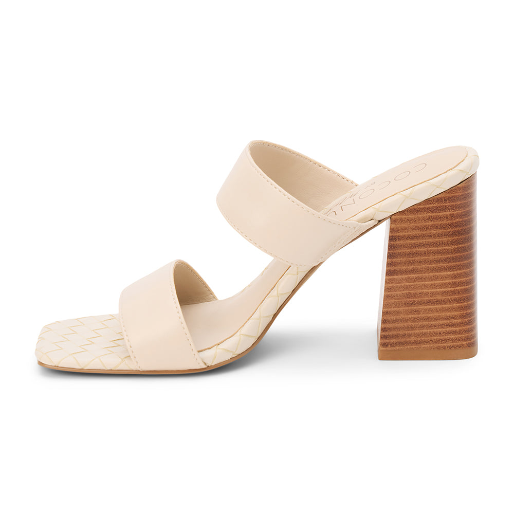 Beige faux leather heeled sandal with wide straps, woven footbed, and tall block heel, shown on a white background.