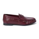 Vegan burgundy faux leather penny loafer with a penny strap, moc-toe stitching, gathered toe detail, and black low heel shown on a white background.
