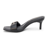 Black faux leather slide sandal with an open square toe, wide buckle strap, mid heel, and slip-on design, shown on a white background.