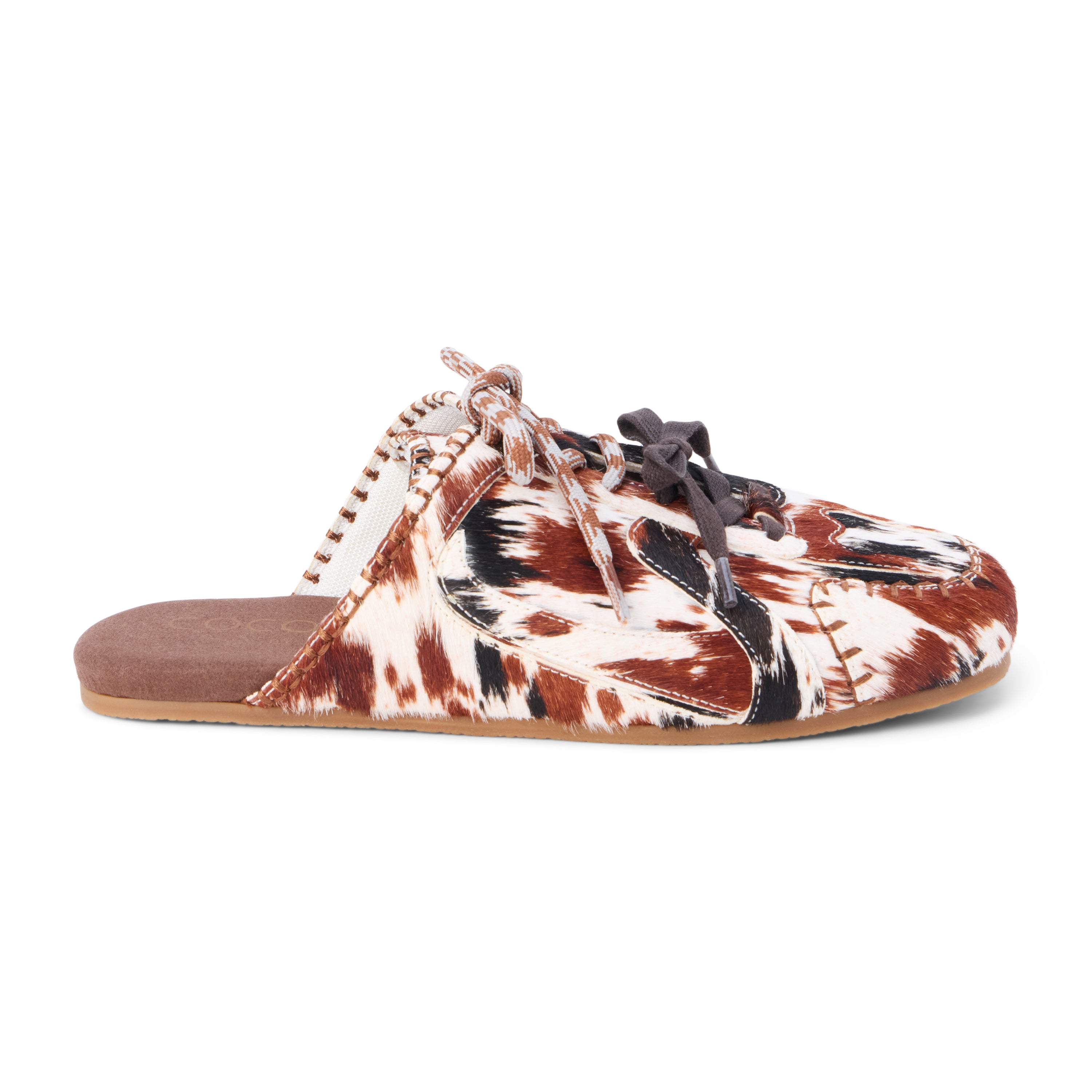 Brown and white cow hair mule with a lace-up front, stitched detailing, flat sole, and open back, shown in side profile on a white background.
