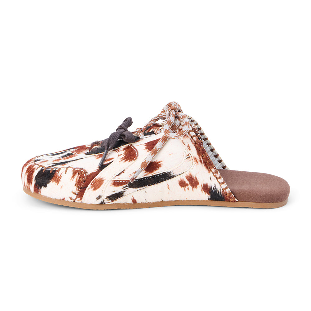 Brown and white cow hair mule with a lace-up front, stitched detailing, flat sole, and open back, shown in side profile on a white background.