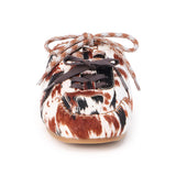 Brown and white cow hair mule with a lace-up front, stitched detailing, flat sole, and open back, shown in side profile on a white background.