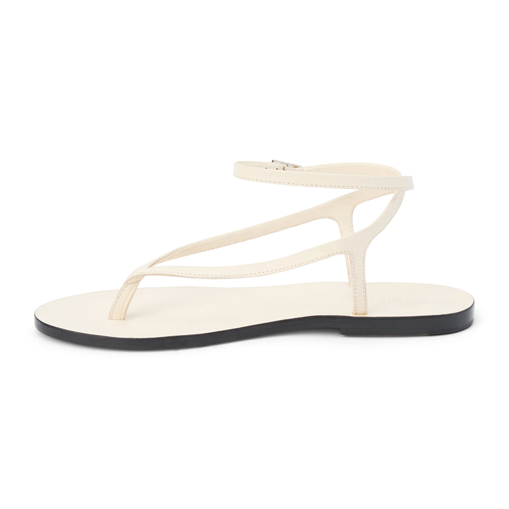 Ivory leather thong sandal with a minimalist strappy design and adjustable ankle buckle. A sleek and versatile style for effortless warm-weather dressing.