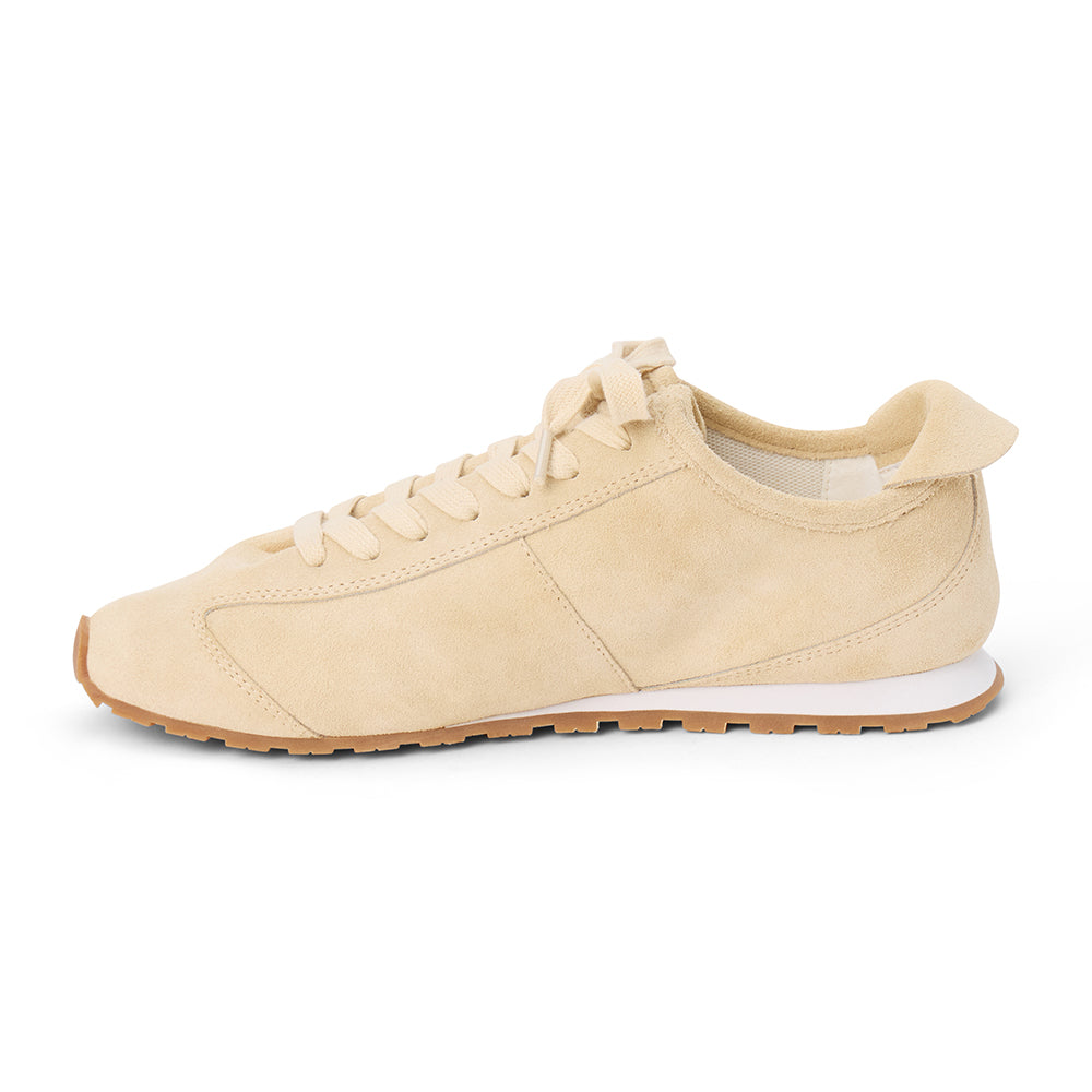 Ivory suede trainer with tonal laces, stitched paneling, a low-profile silhouette, white midsole, and gum outsole shown on a white background.