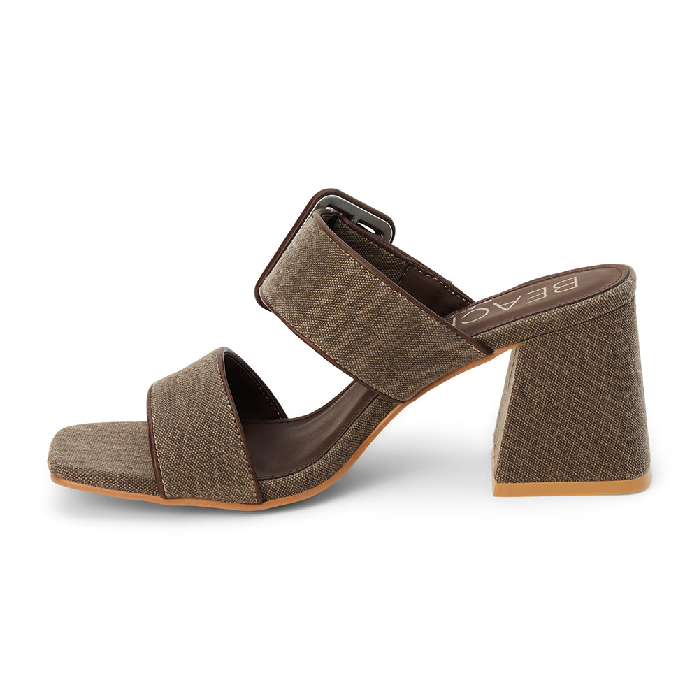 Chocolate textile heeled sandal with a wide textured strap, oversized buckle detail, square toe, and block heel, shown on a white background.