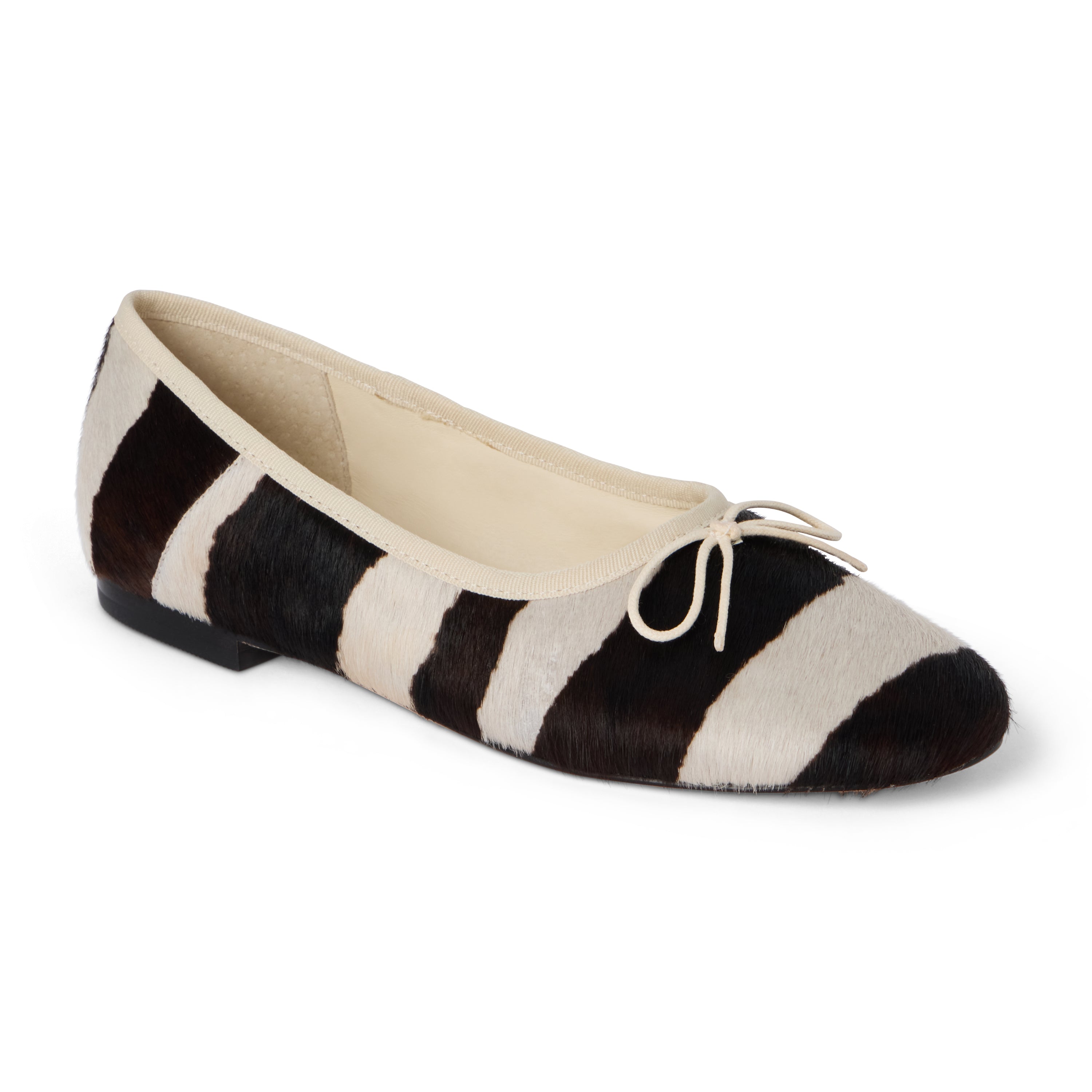Ivory and dark brown zebra-print cow hair ballet flat with an ivory bow, rounded toe, tonal trim, and low heel shown on a white background.