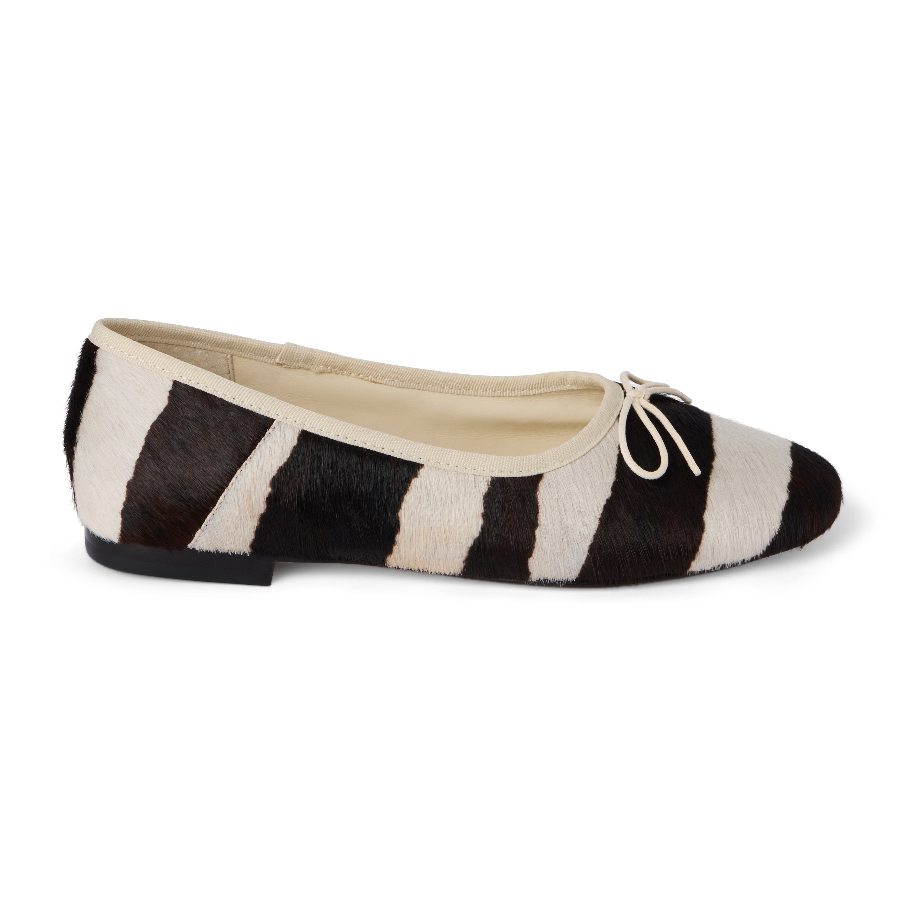 Ivory and dark brown zebra-print cow hair ballet flat with an ivory bow, rounded toe, tonal trim, and low heel shown on a white background.