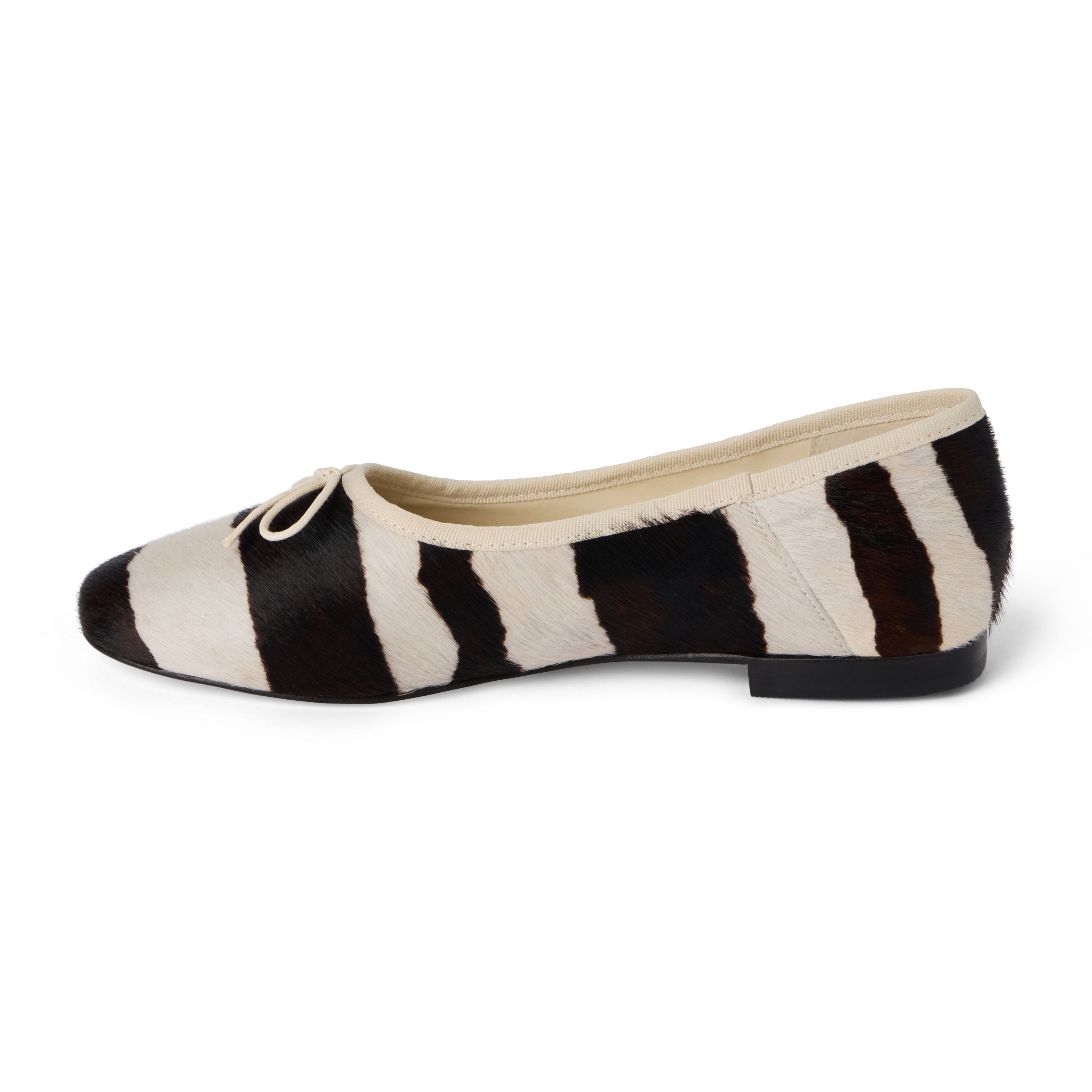 Ivory and dark brown zebra-print cow hair ballet flat with an ivory bow, rounded toe, tonal trim, and low heel shown on a white background.