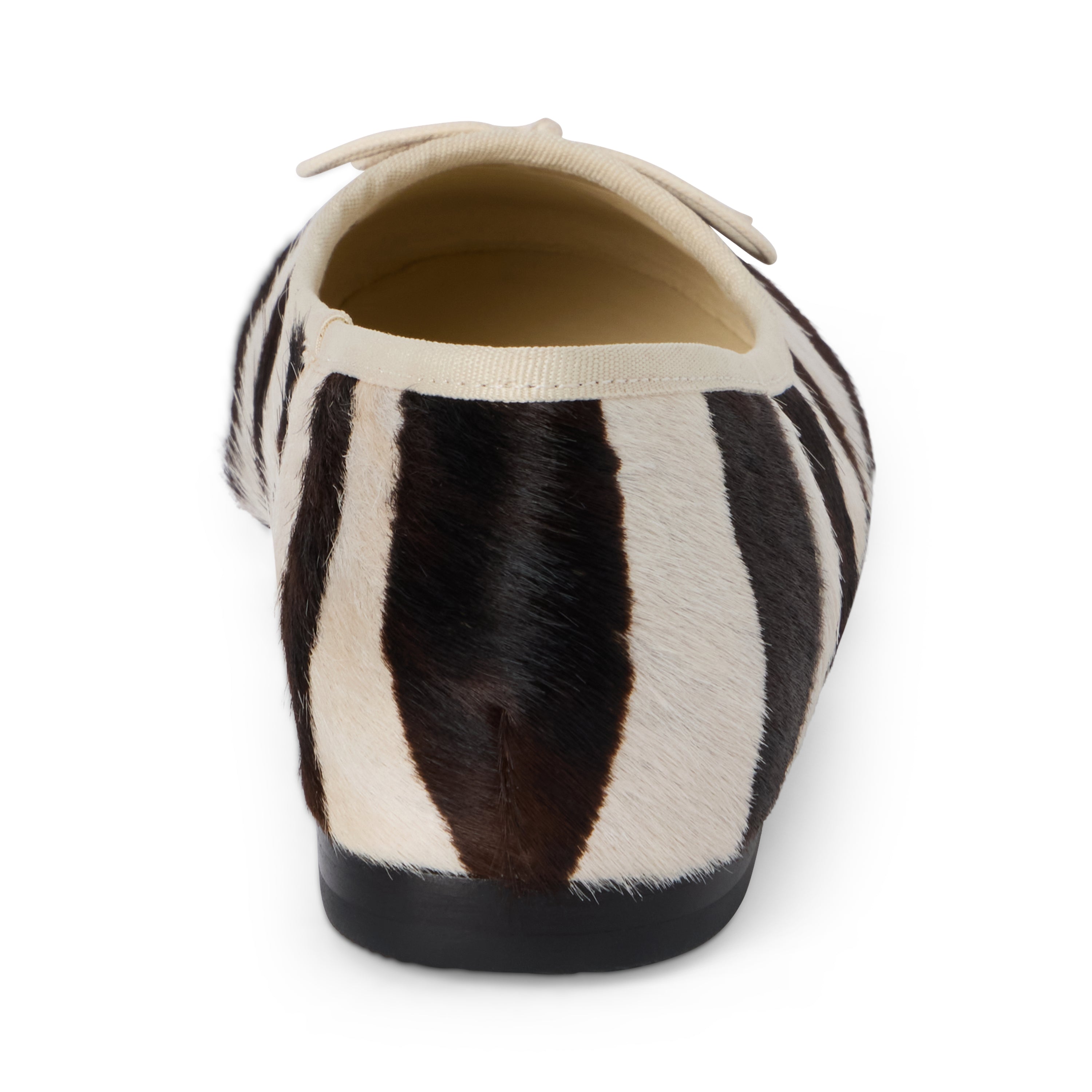 Ivory and dark brown zebra-print cow hair ballet flat with an ivory bow, rounded toe, tonal trim, and low heel shown on a white background.