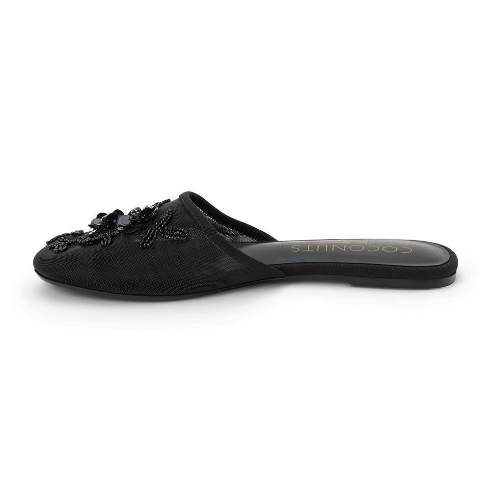 Black mesh mule with floral embellishments, slip-on design, low flat sole, and pointed toe, shown on a white background.