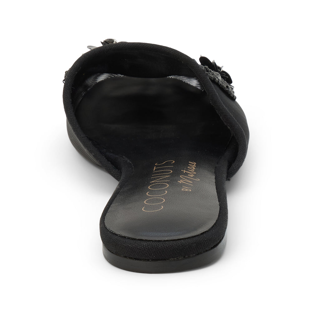 Black mesh mule with floral embellishments, slip-on design, low flat sole, and pointed toe, shown on a white background.