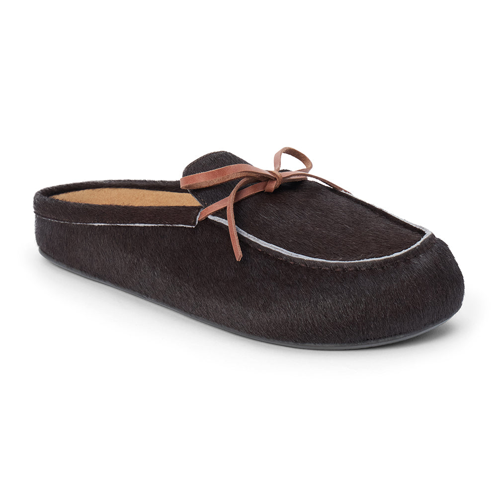 Dark brown cow hair clog with a moc-style apron toe, decorative leather bow, and backless silhouette shown on a white background.