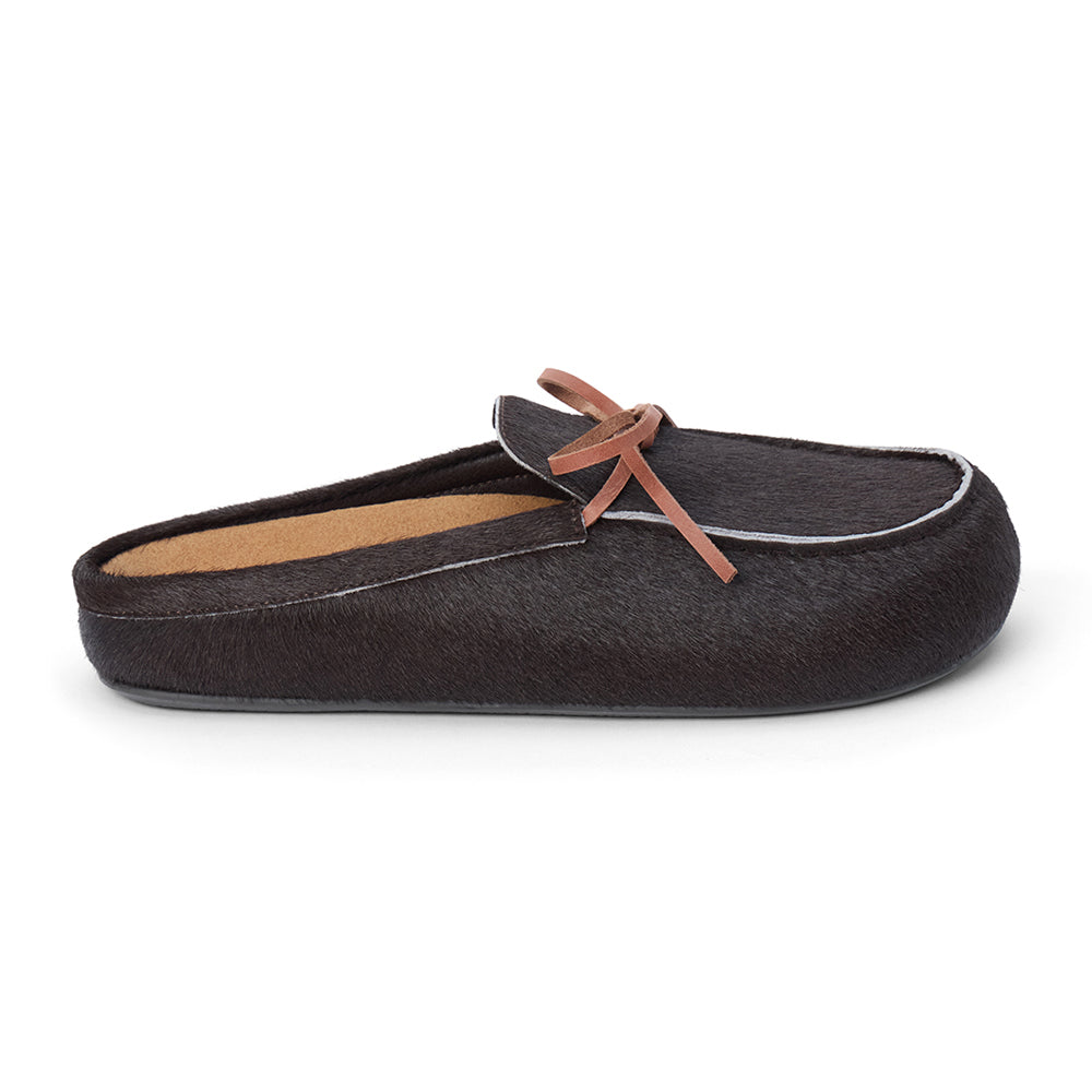 Dark brown cow hair clog with a moc-style apron toe, decorative leather bow, and backless silhouette shown on a white background.