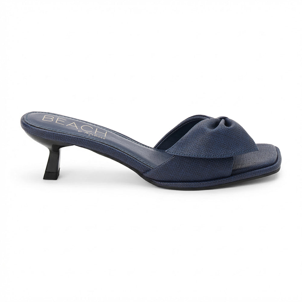 Navy vegan faux leather heeled sandal with knotted bow detail and slim heel, shown on a white background.