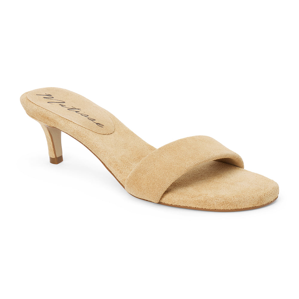 Beige suede slide sandal with wide strap and low kitten heel, shown on a white background.