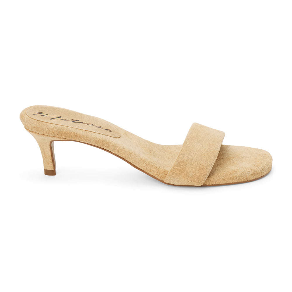 Beige suede slide sandal with wide strap and low kitten heel, shown on a white background.