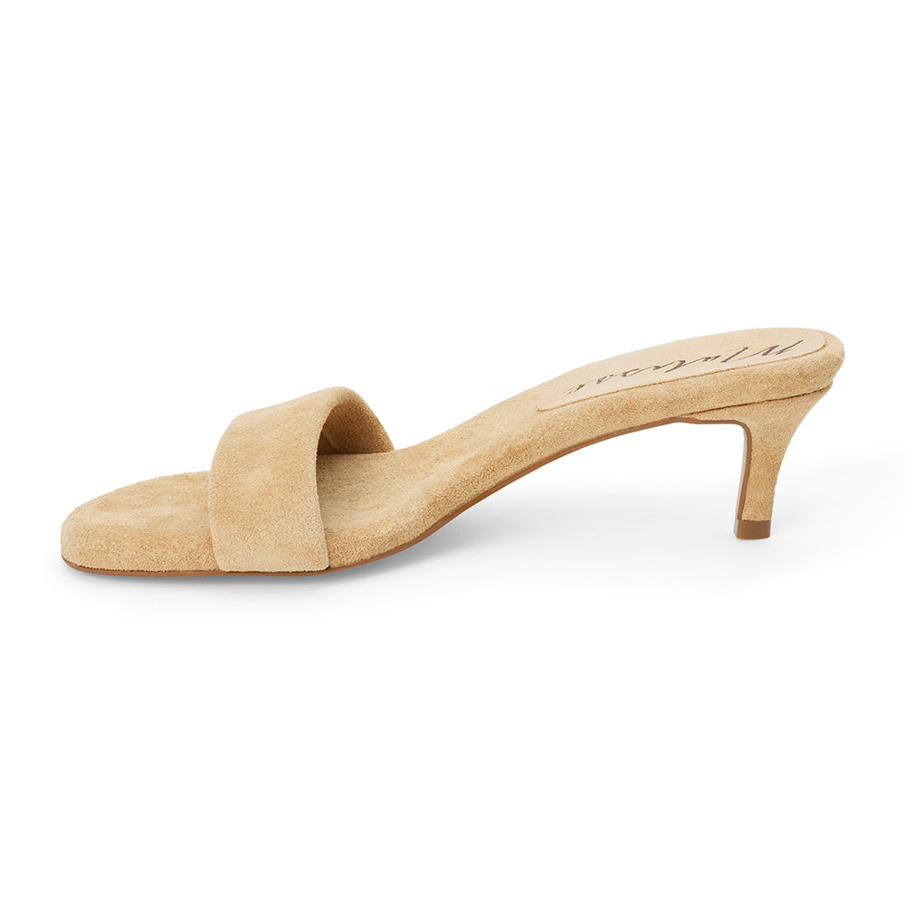 Beige suede slide sandal with wide strap and low kitten heel, shown on a white background.