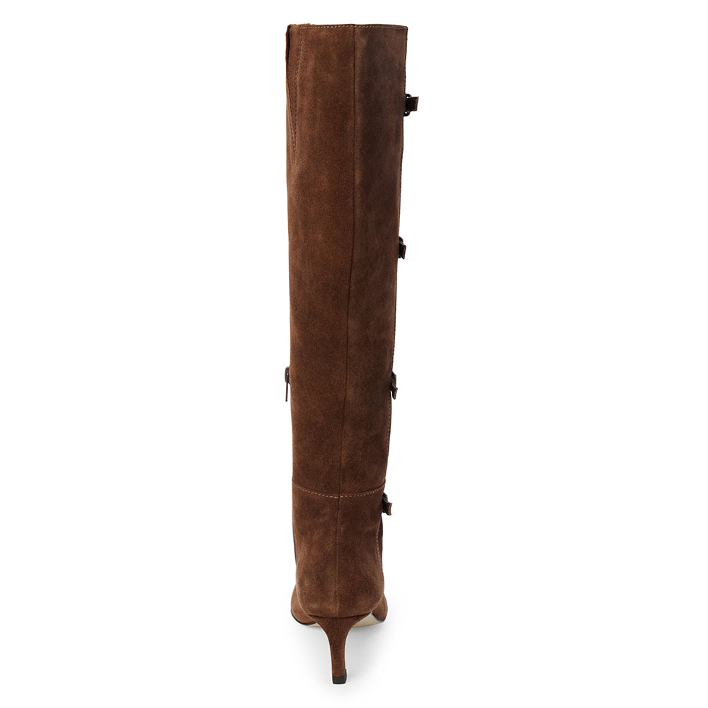 Brown suede knee-high boot with four silver-tone buckle accents, a pointed toe, and slim brown kitten heel shown on a white background.
