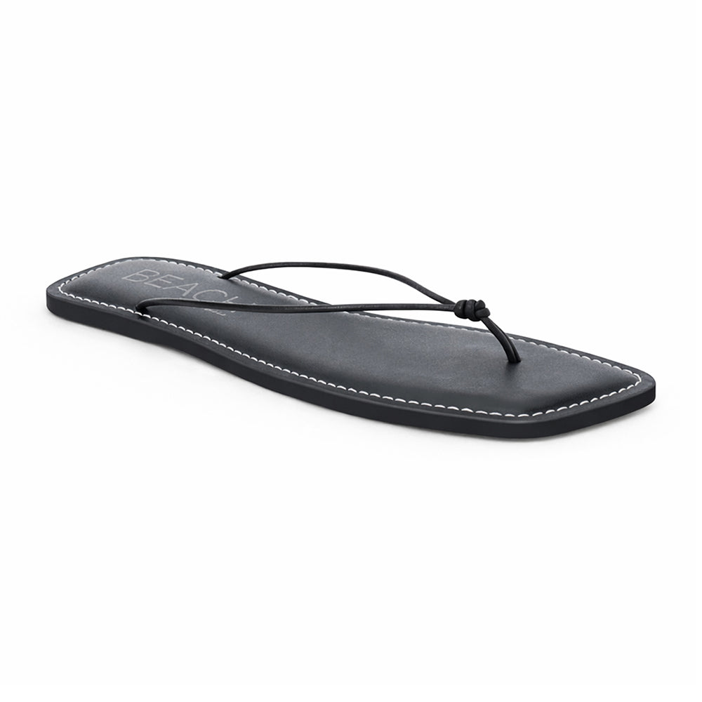Black leather flat thong sandal with slim knotted straps and square toe, shown on a white background.