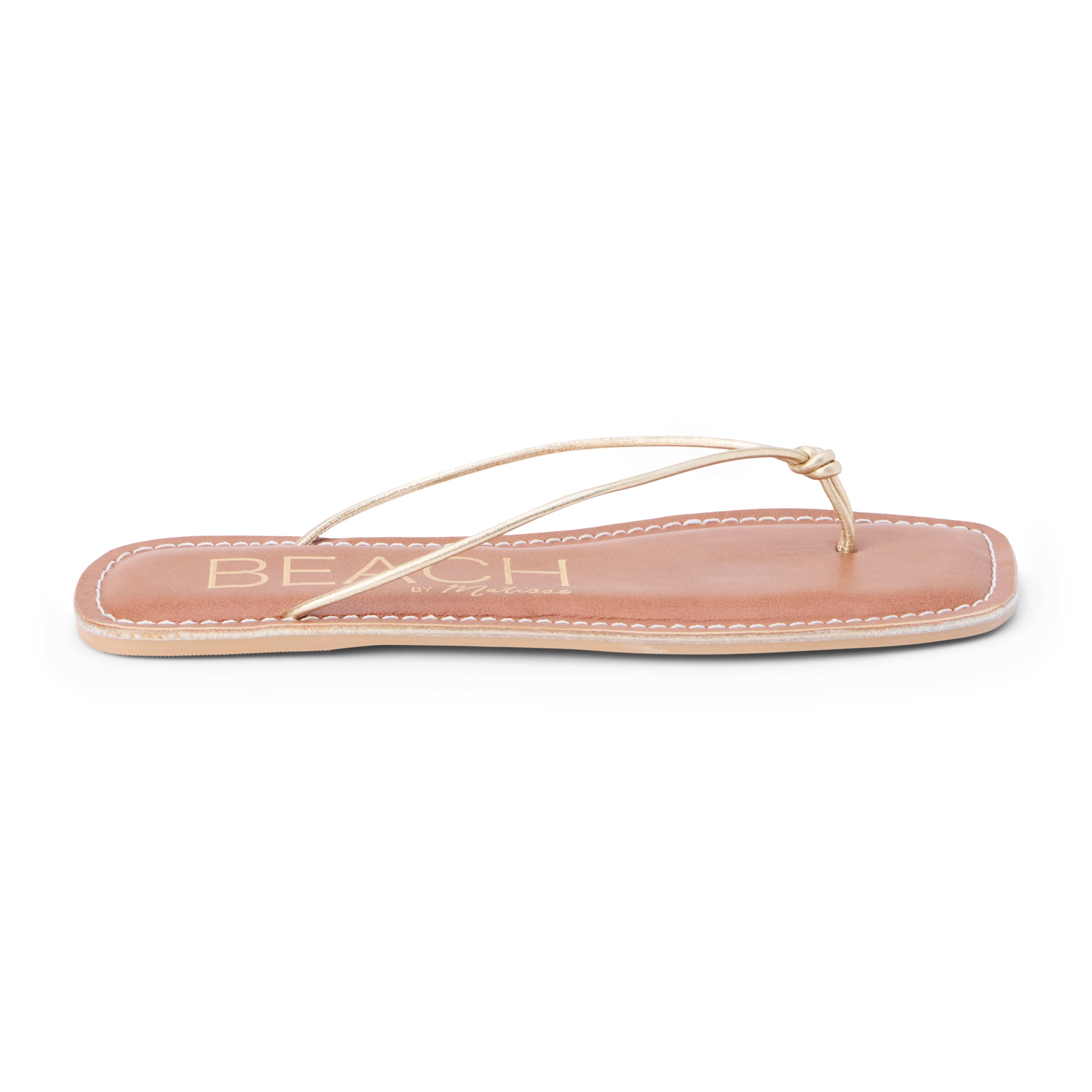 Metallic gold leather flat thong sandal with slim knotted straps and square toe, shown on a white background.